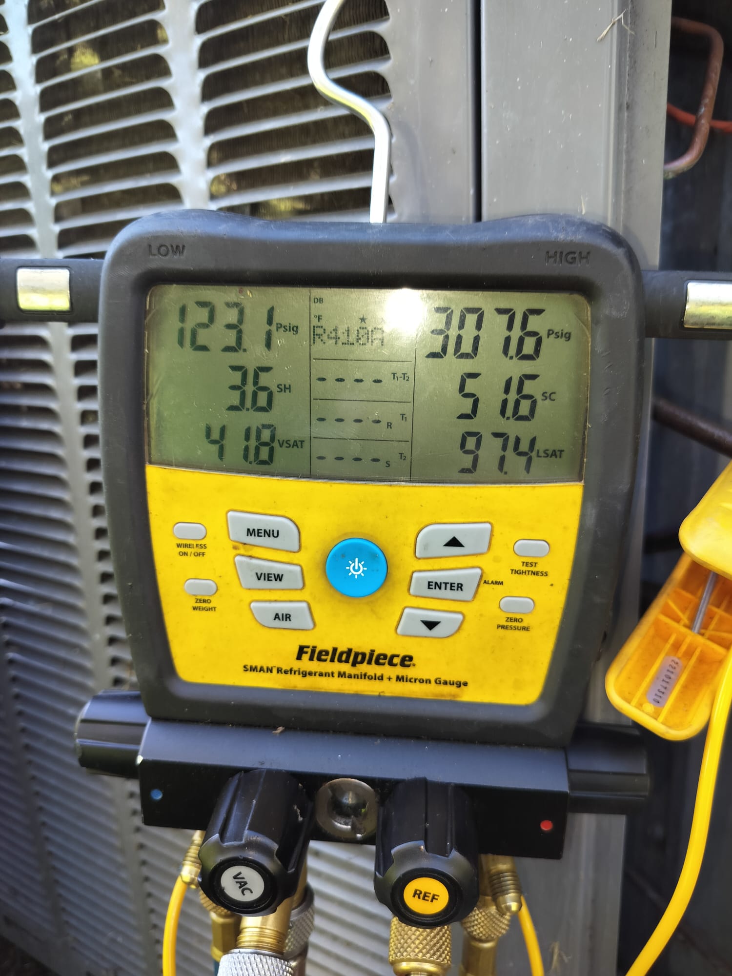 Digital refrigerant gauge hooked up to an outdoor HVAC unit for a pressure check