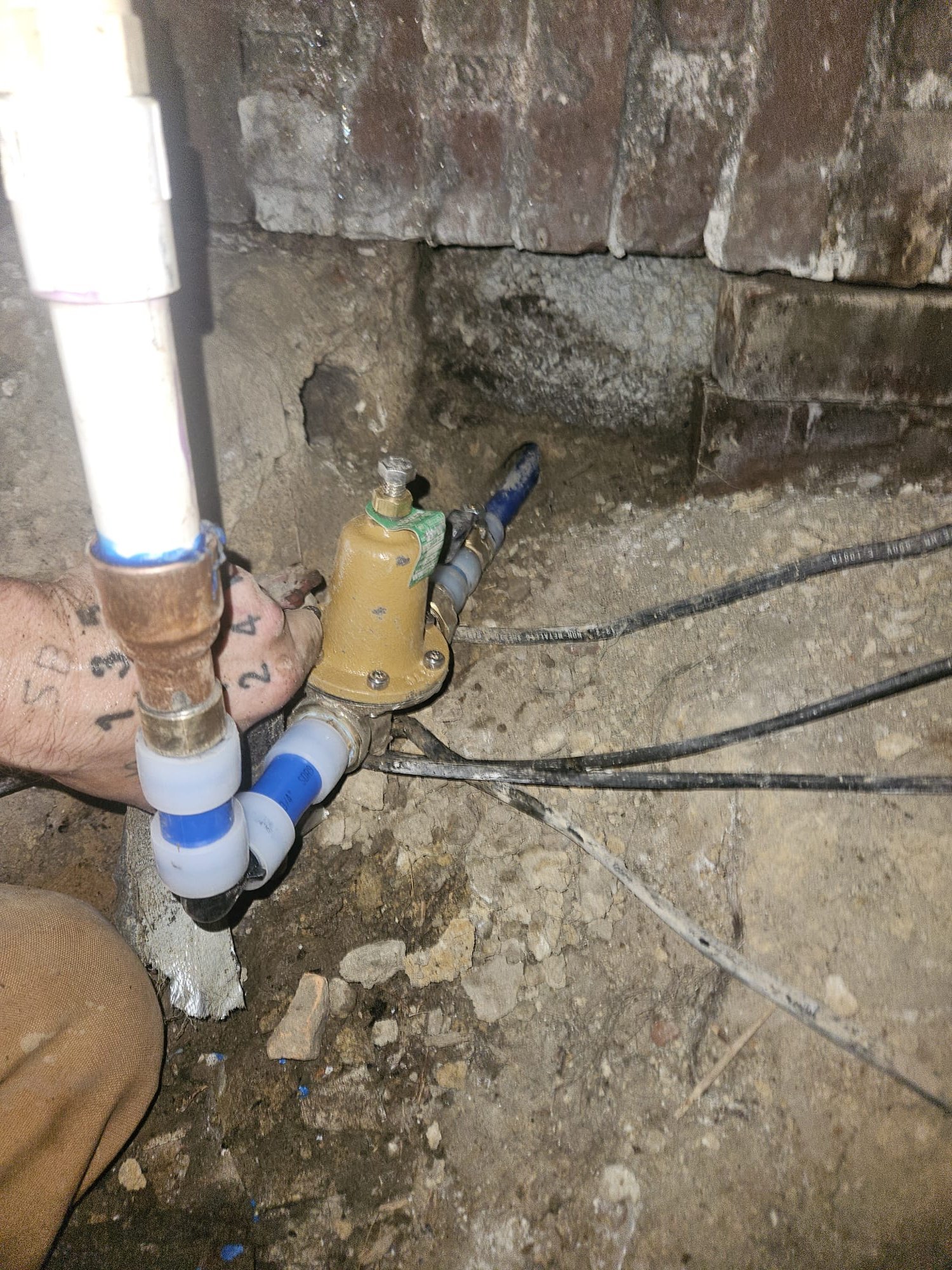 A HEP technician installing a pressure regulator in a crawl space