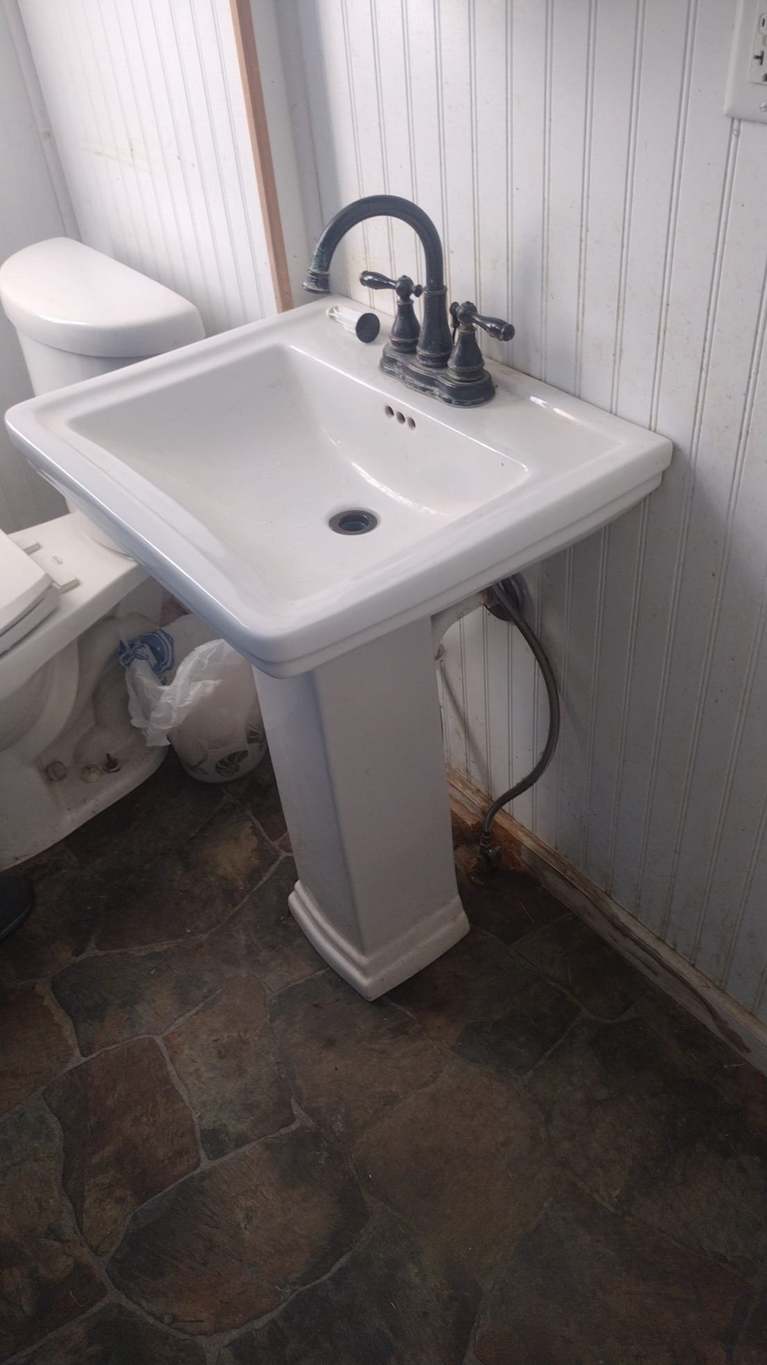 Older pedestal sink with signs of moisture and missing drain stopper