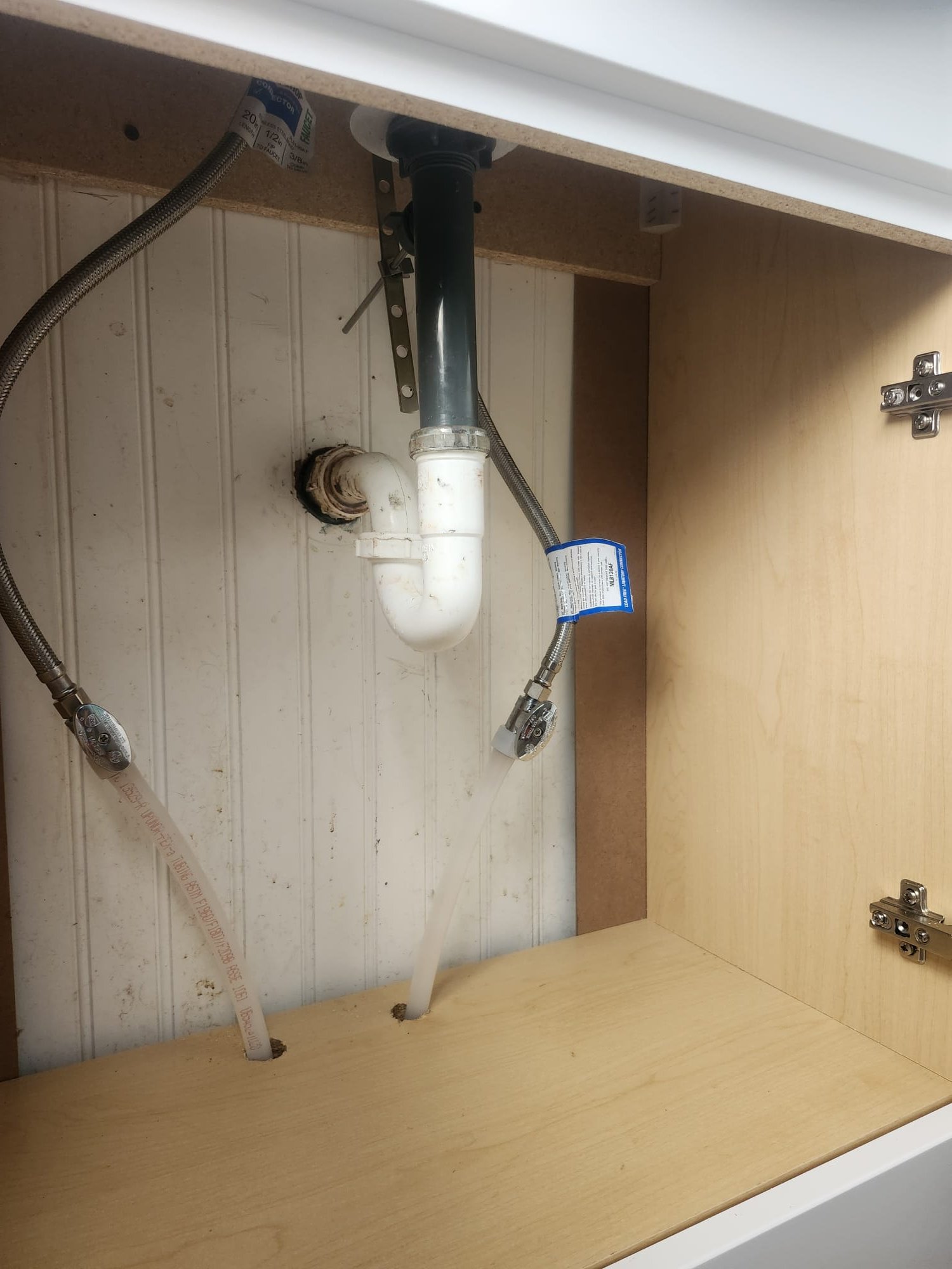 Under-sink plumbing after installation, highlighting the P-trap and supply lines