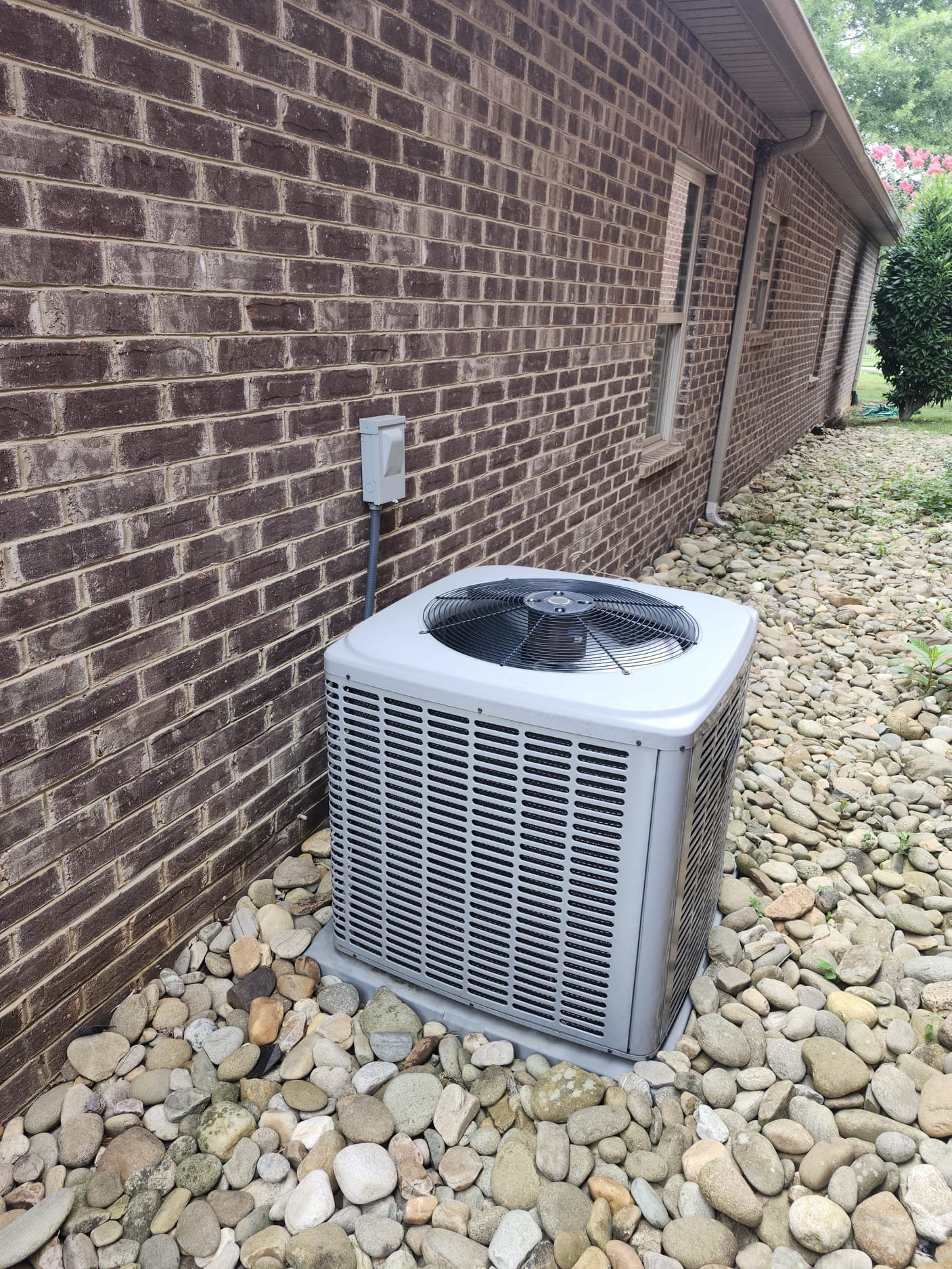 Newly installed outdoor HVAC condenser unit next to a brick home, set on a stable pad and surrounded by clean landscaping rocks.