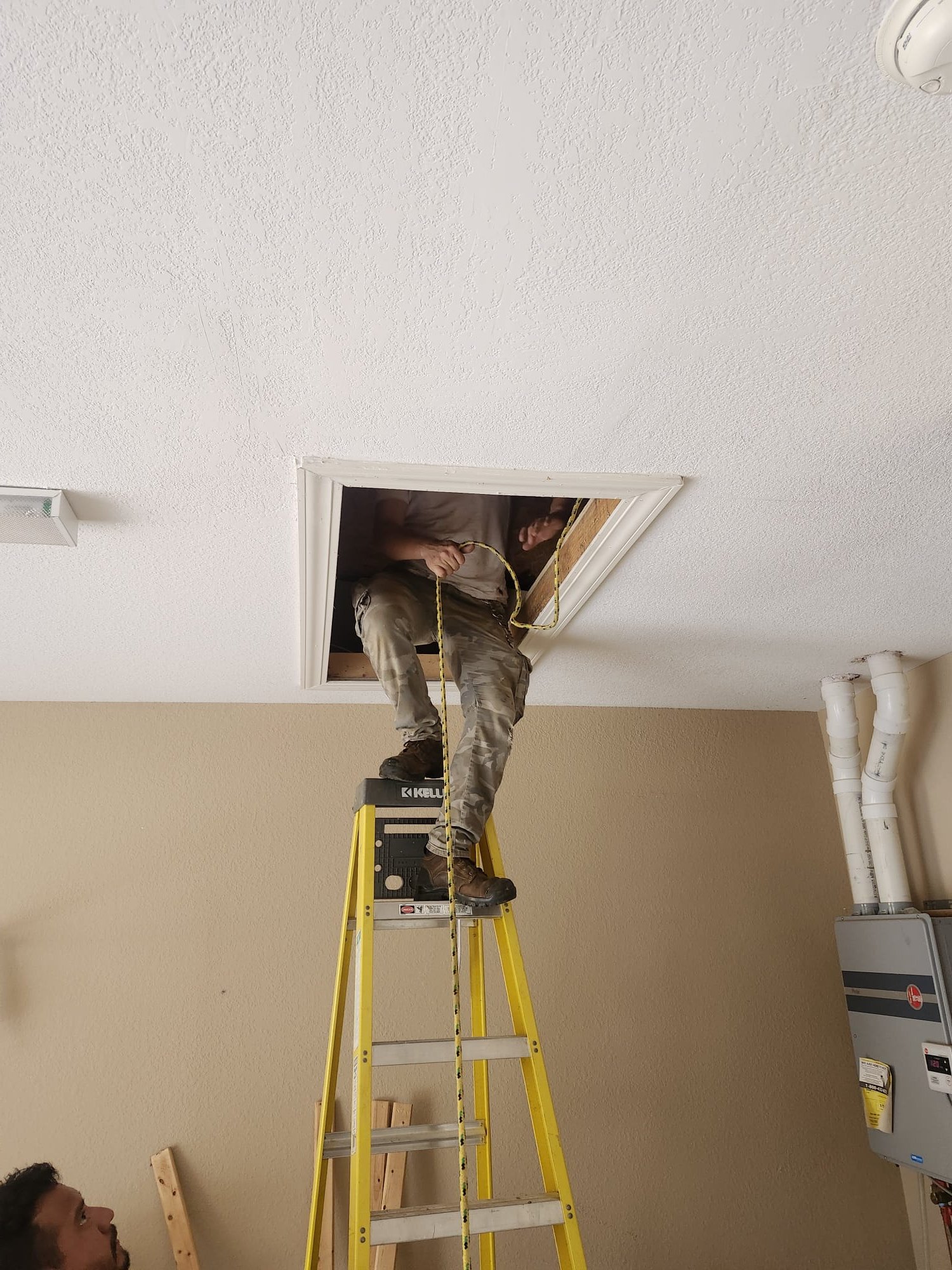 A HEP technician working in an attic access point, using a ladder to safely install HVAC components.