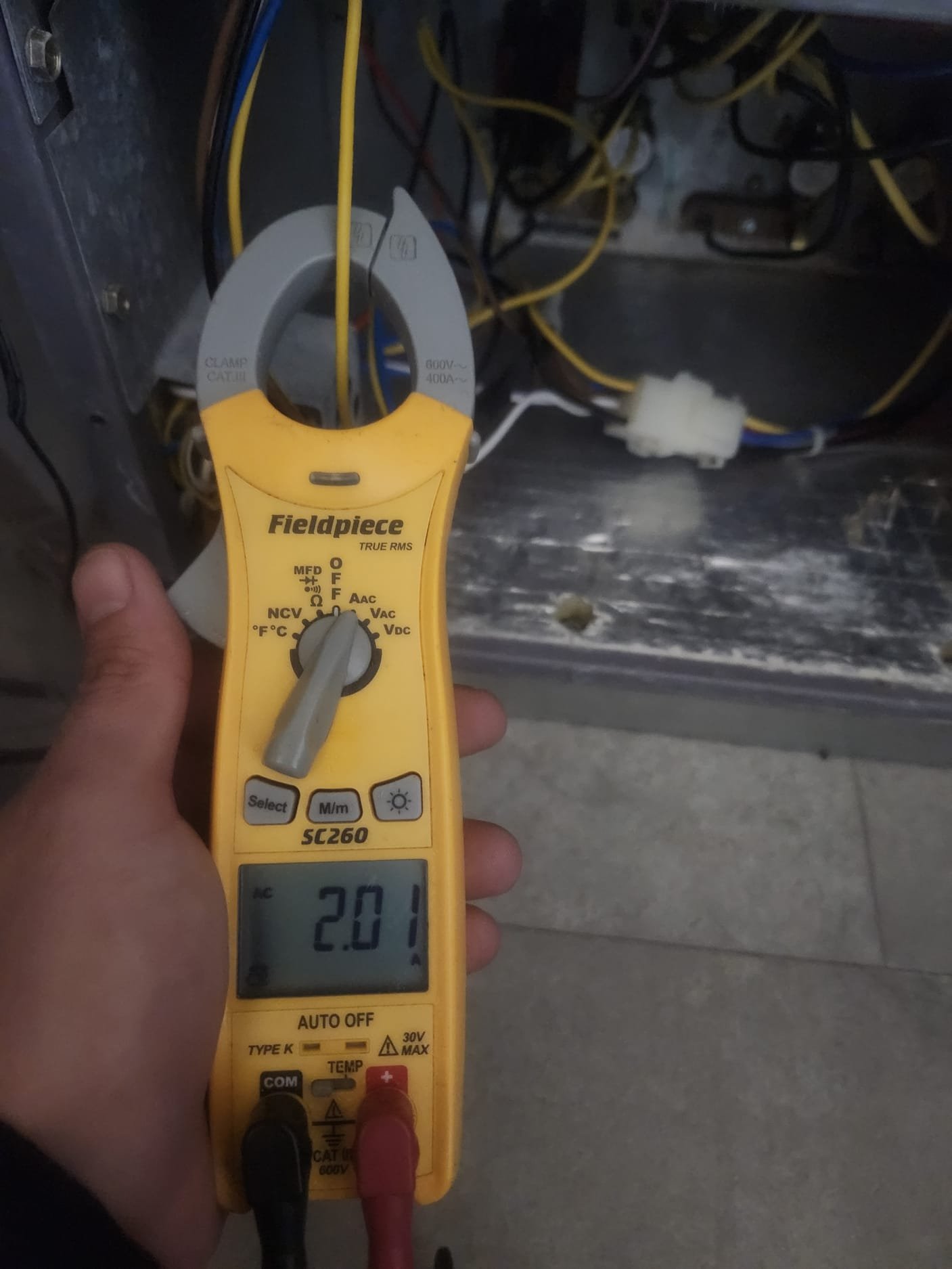 Clamp meter measuring electrical current around a wire inside an HVAC unit. The reading helps ensure electrical components are running smoothly.