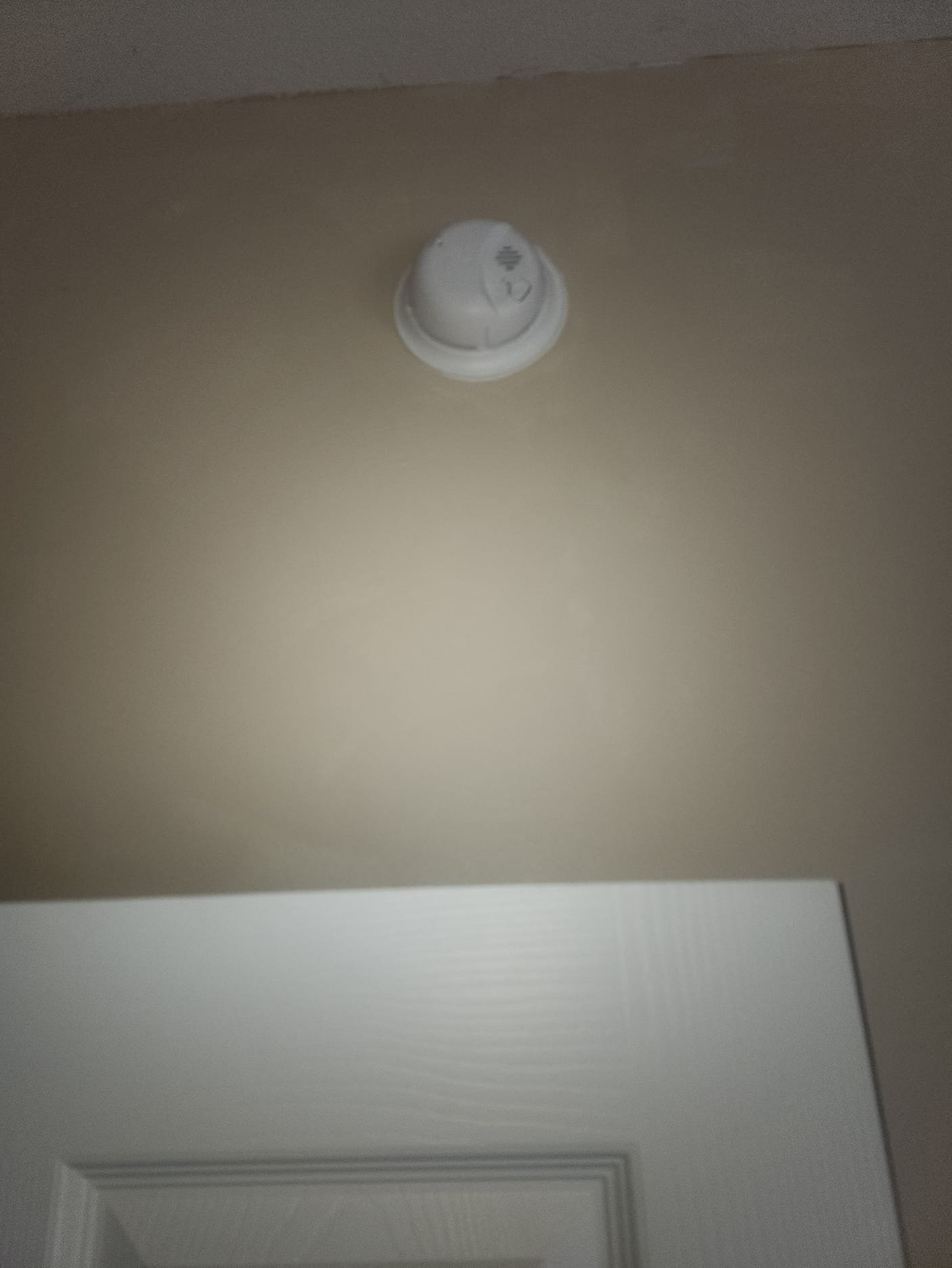 A newly installed smoke detector in pristine condition, properly mounted just above a door frame.