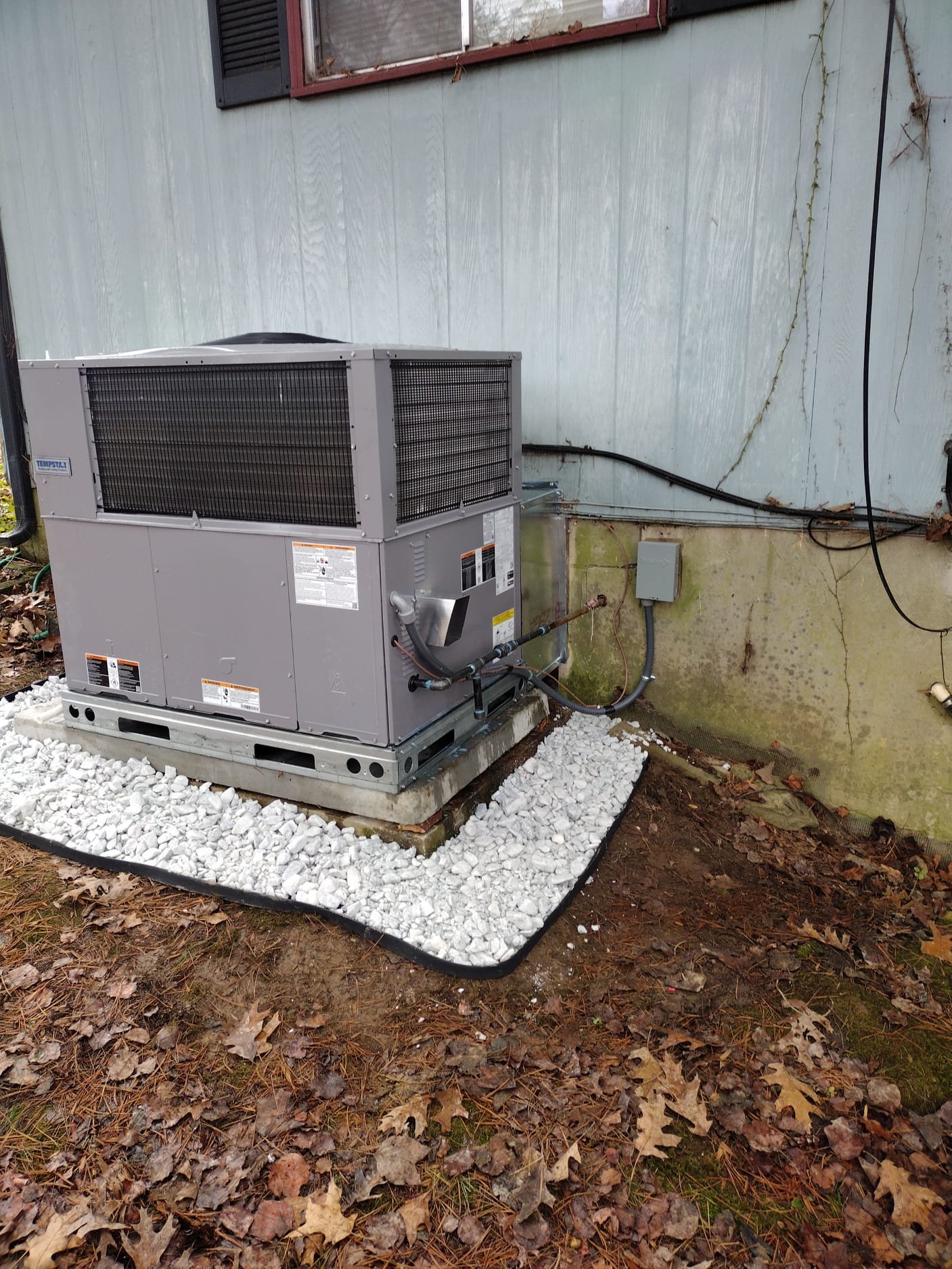 Brand-new HVAC system mounted on a sturdy base with fresh gravel bed.
