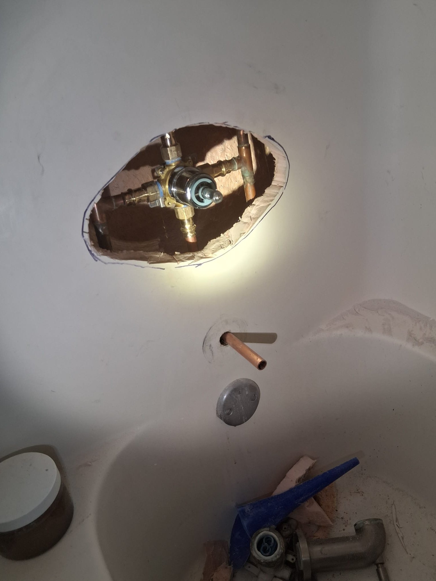 This image shows a bathtub plumbing installation in progress. The wall above the bathtub has been cut open to expose the plumbing behind it. Inside the opening, you can see a newly installed brass shower valve connected to copper pipes. The clean, shiny appearance of the valve and fittings indicates that these components are new.