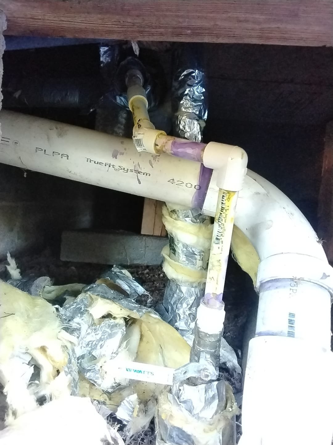 Section of plumbing with torn insulation in a crawl space