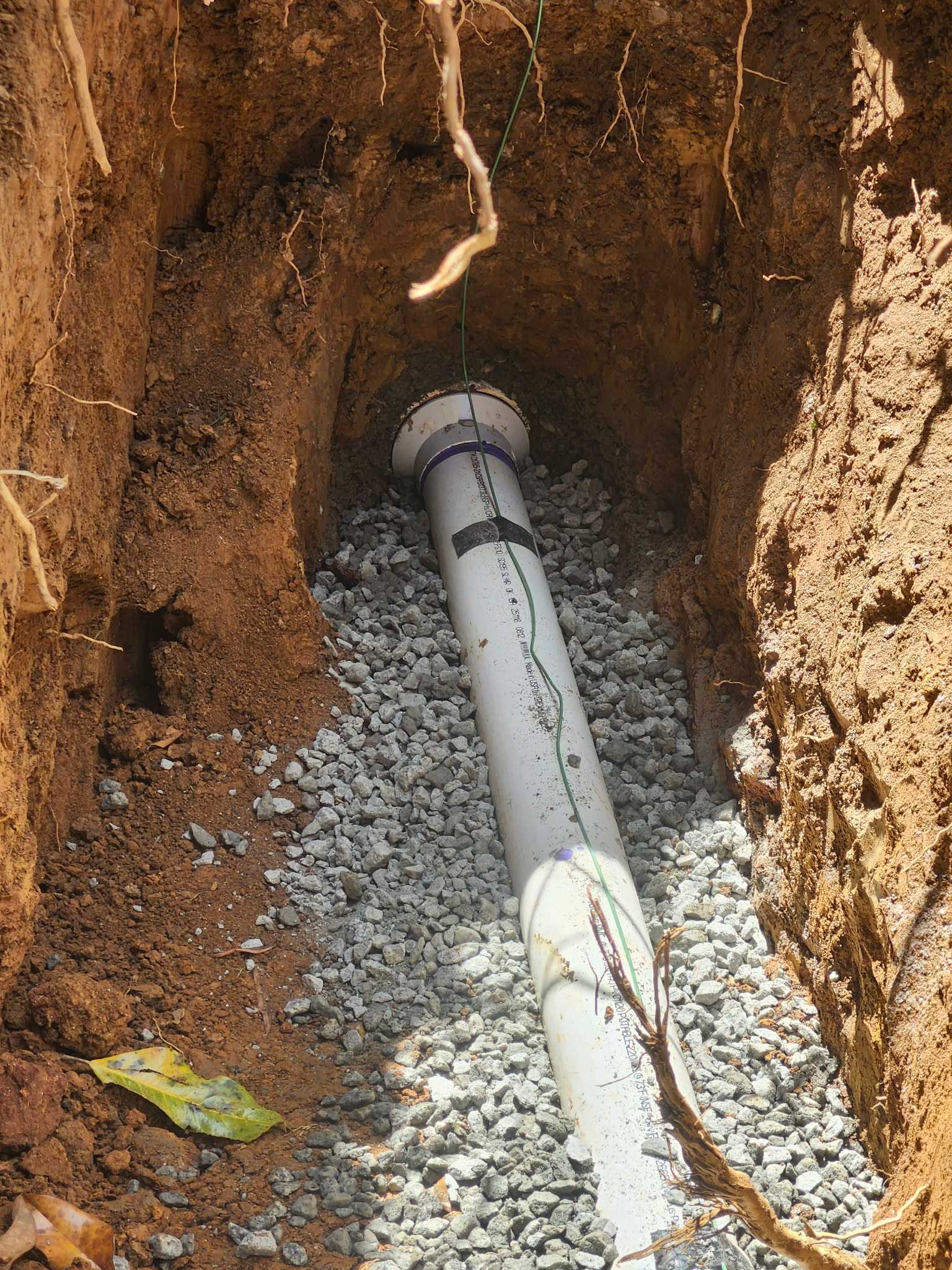 Close-up of a newly installed sewer pipe with primer marks, gravel bedding, and tracer wire