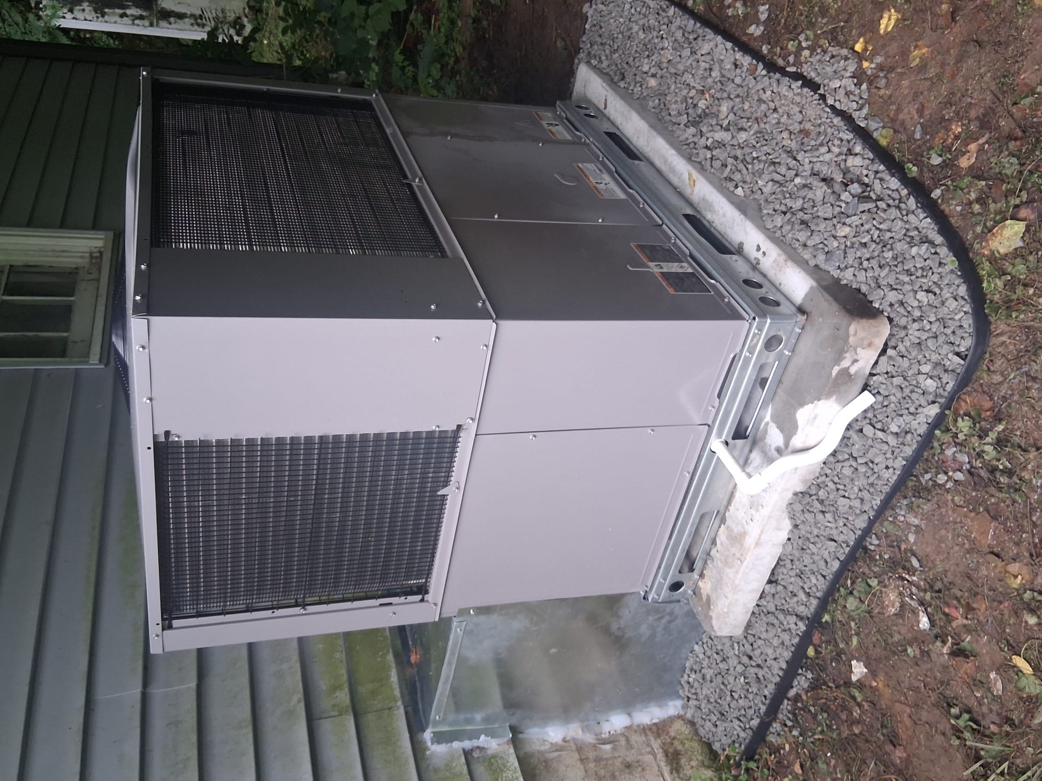 Newly installed packaged HVAC unit on a concrete pad surrounded by gravel.