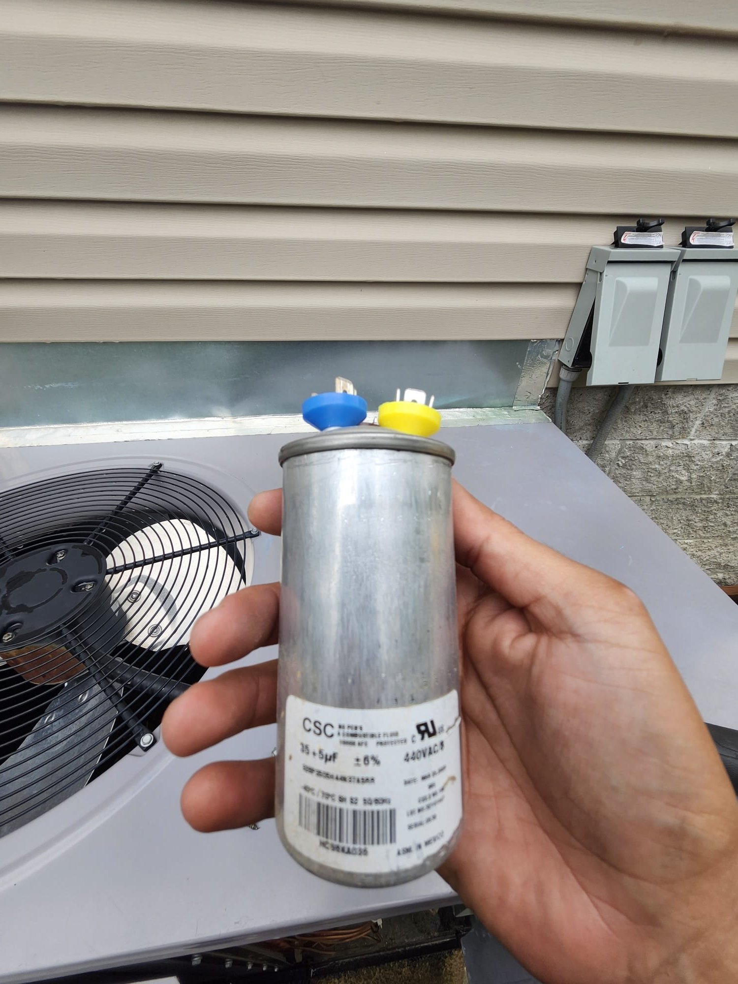 A technician holding an HVAC capacitor during service