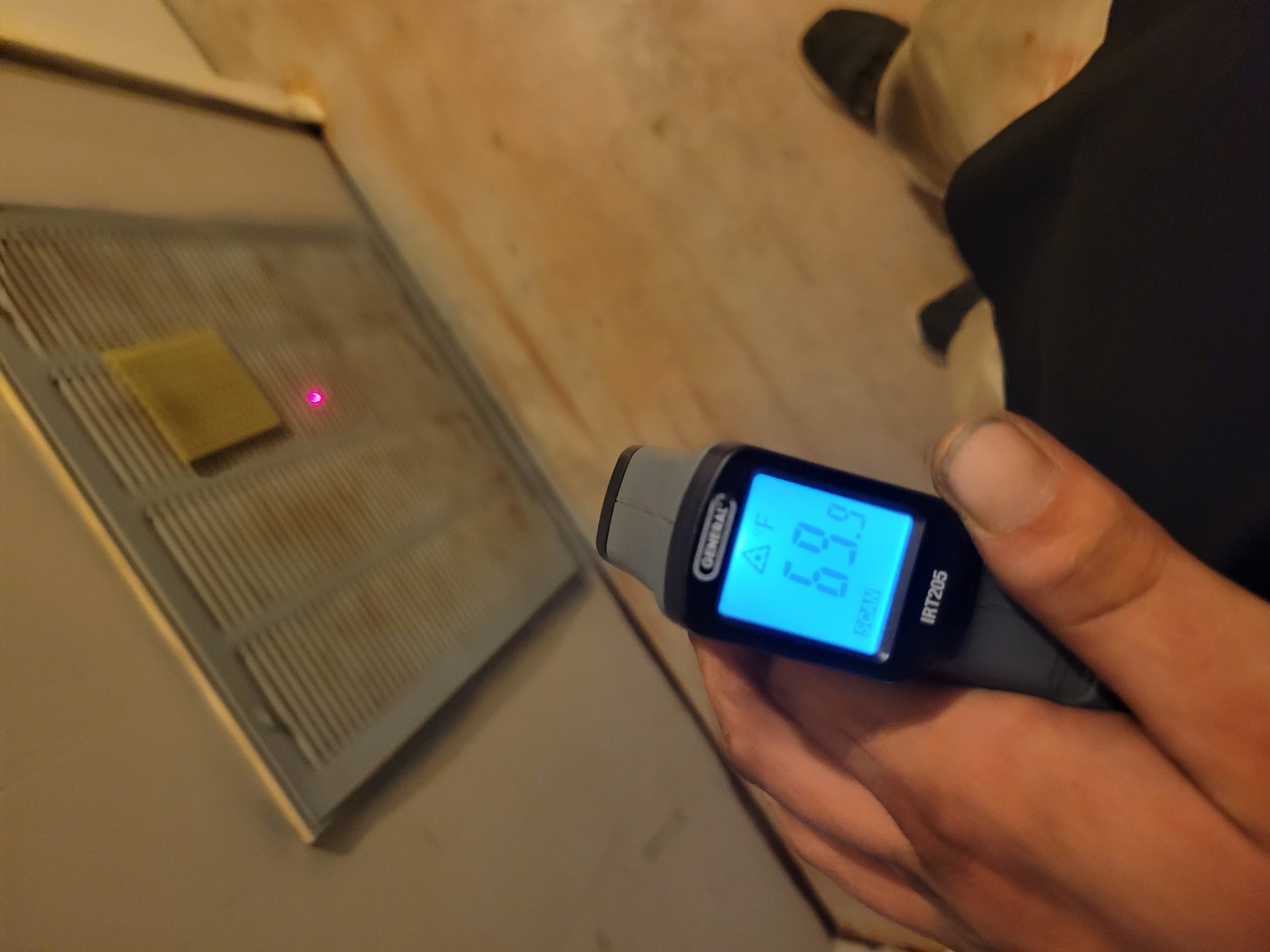 Technician checking air temperature at a vent during HVAC service