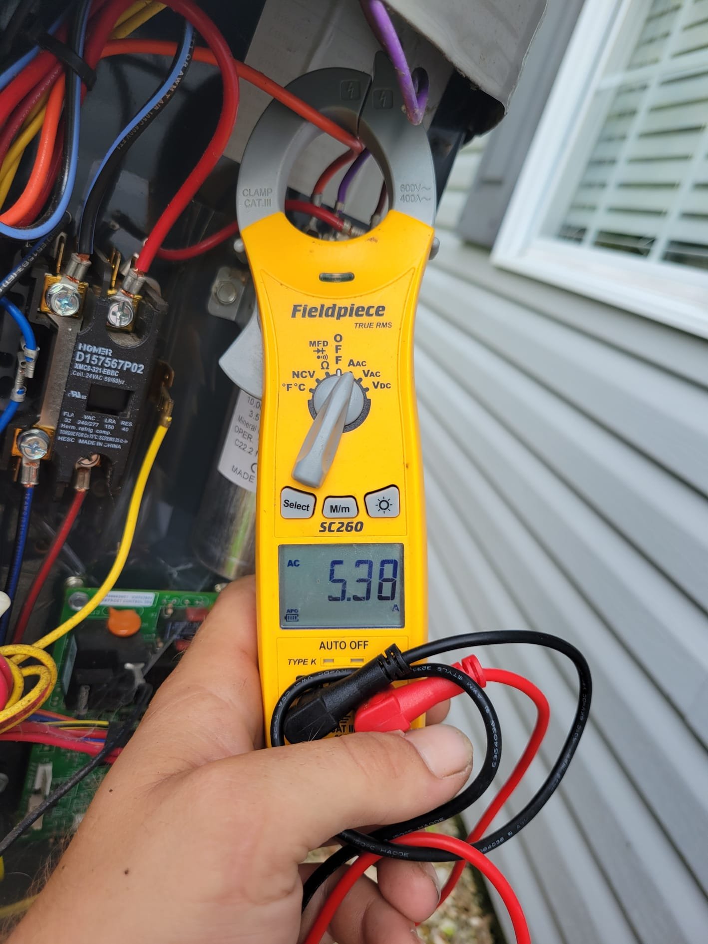 A HEP technician checking electrical draw inside an outdoor HVAC unit