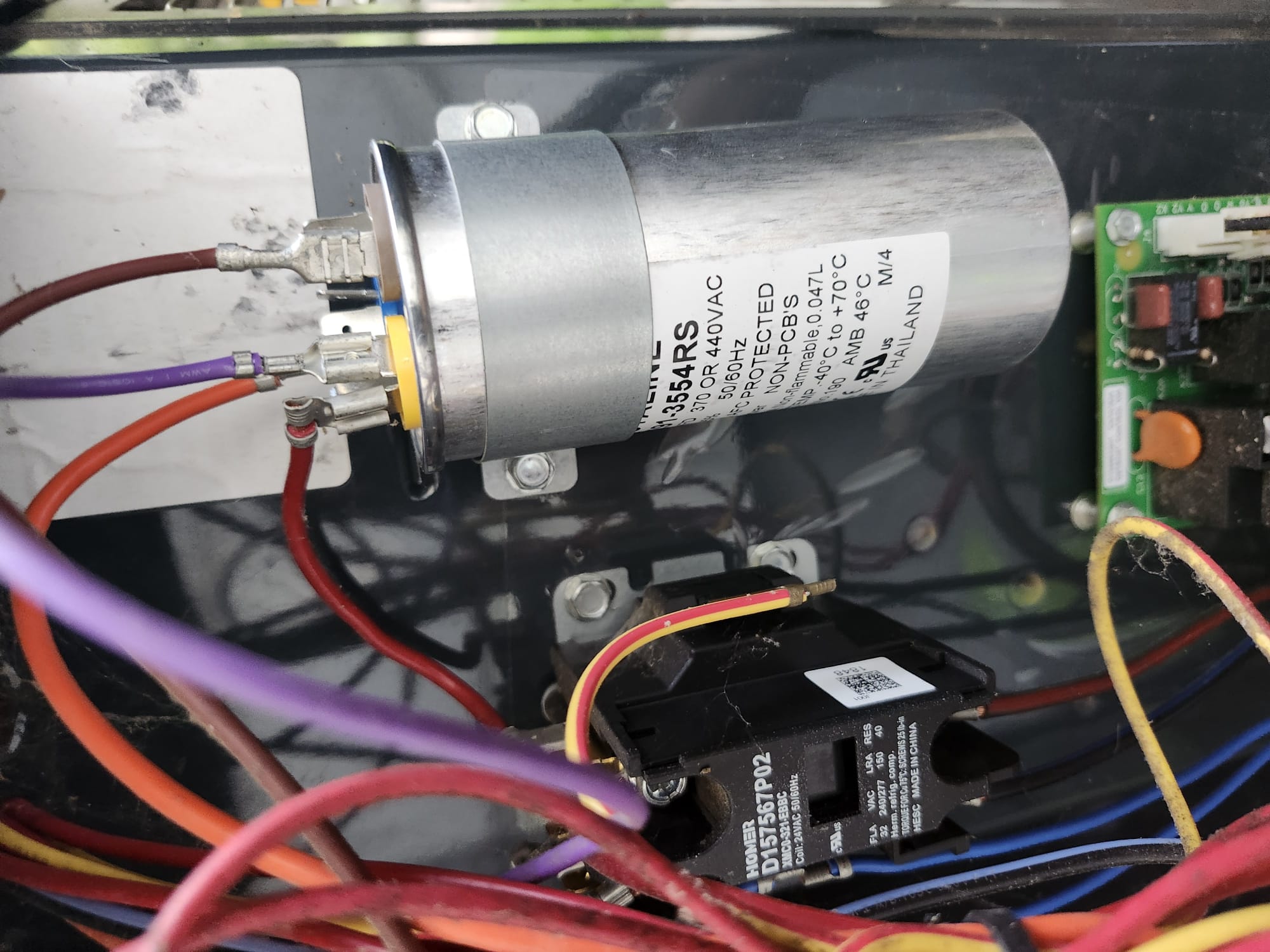 An HVAC electrical compartment with a recently replaced capacitor, wiring, and control parts inside the outdoor unit.