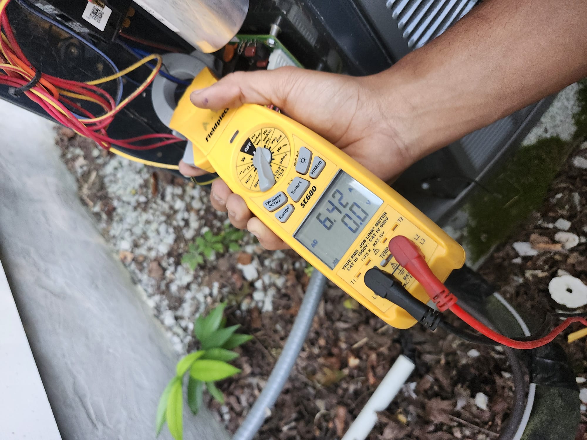 A HEP technician testing electrical readings on an outdoor HVAC unit during a service visit.